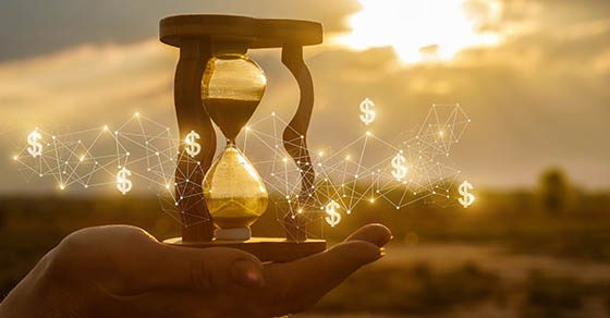 The concept of time and the new financial ideas. Hourglass in hand with and financial structure at sunset. | Series EE Savings Bond Taxation | Dalby Wendland & CO. | CPAs | Business Advisors | Colorado